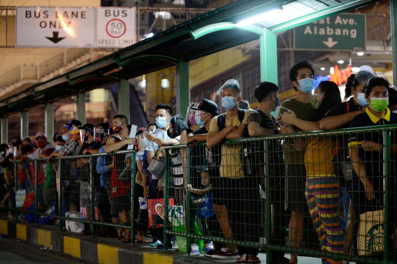 People wearing face masks and face shields as protection against the coronavirus disease queue at a bus stop, in Quezon City, Metro Manila, Philippines on December 23, 2020.