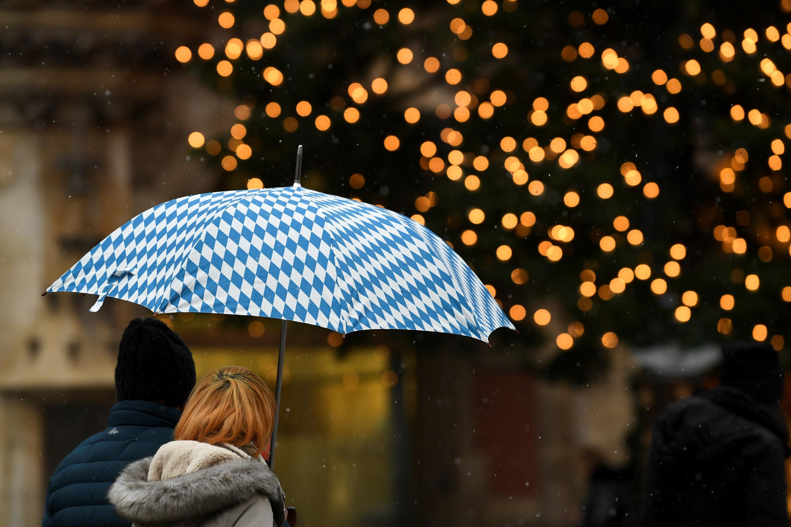 A couple with an umbrella in the colors of the Bavarian flag pass by a Christmas tree on Marienplatz as the spread of the coronavirus disease (COVID-19) continues in Munich, Germany, December 9, 2020.