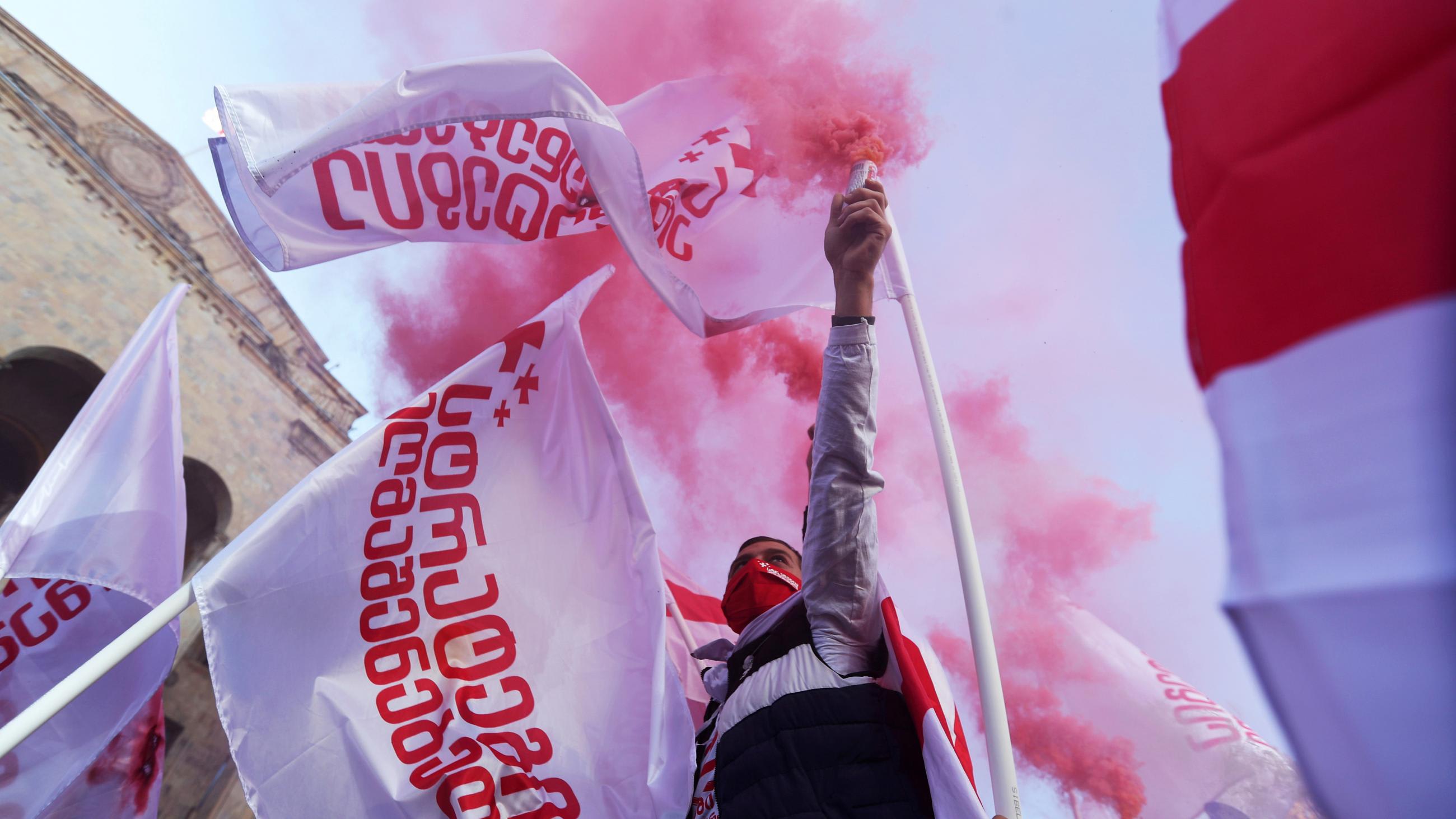An opposition supporter holds a flare releasing red smoke, surrounded by Georgian flags, during a rally against the results of a parliamentary election in Tbilisi, Georgia, on November 8, 2020.