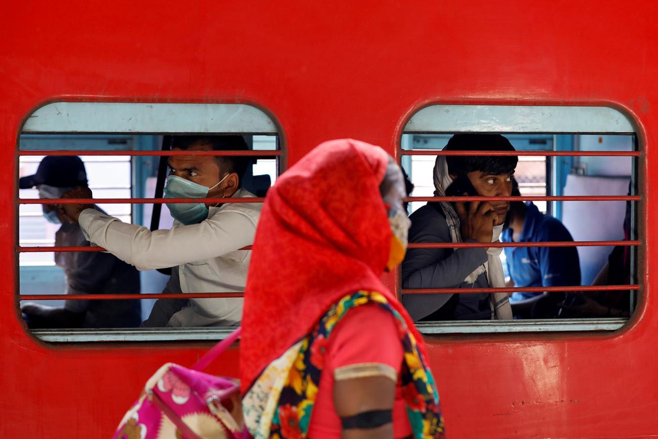 The image shows a bright red train with people inside and a woman walking by the train outside.