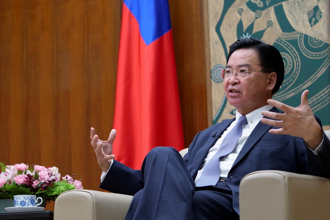 The photo shows the minister seated in a comfortable chair looking off-camera and talking with a serious look on his face and gesturing with his hands.