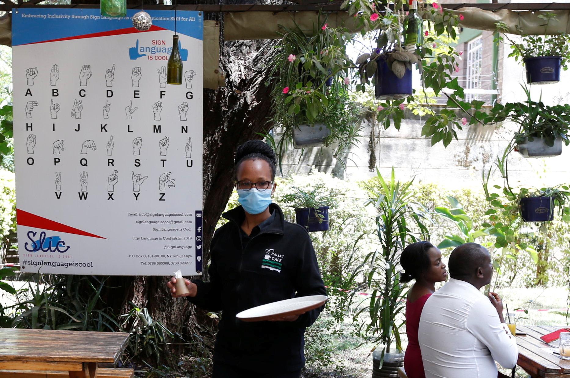 Deaf waitress Sharon Cherono walks past a sign language poster at the Pallet Cafe amid the COVID-19 pandemic, in the Lavington area of Nairobi, Kenya, on August 23, 2021.