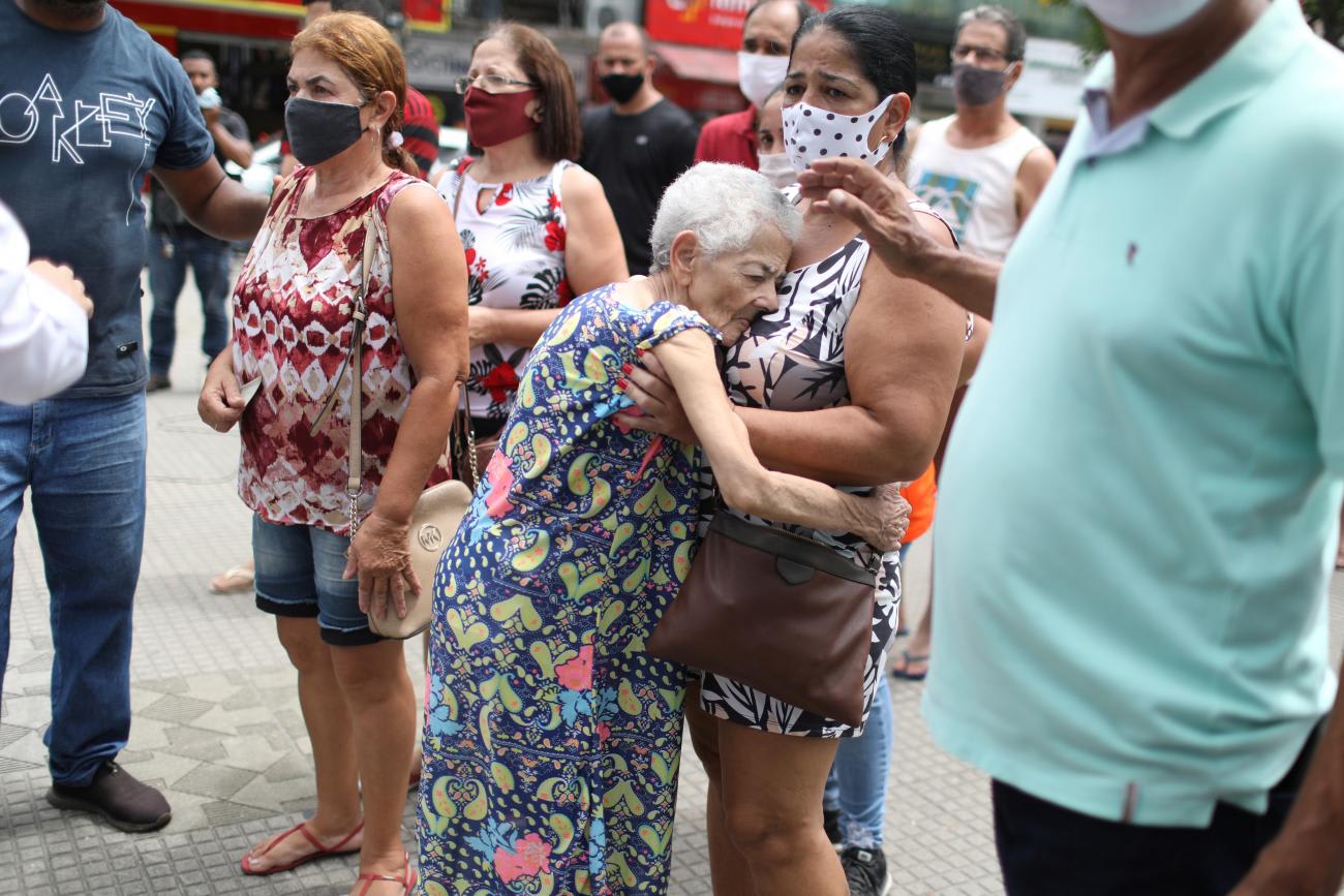 Eliane Paes Leme stands in a crowd of people in colorful clothes holding her mother Tereza de Rosa Paes Leme, 83. Leme is wearing a blue floral dress, who has Alzheimer's disease, after she received the first dose of Sinovac's CoronaVac COVID-19 vaccine for senior citizens, in Duque de Caxias, Rio de Janeiro state, Brazil March 5, 2021.