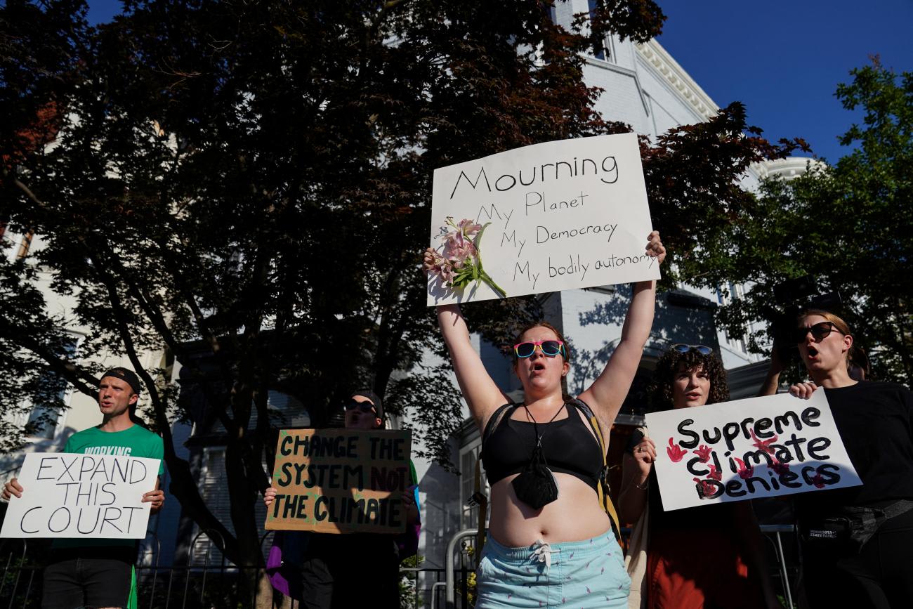 A female protestor wearing a black crop top holds up a white signs that reads "Mourning my planet, my democracy, my bodily autonomy"