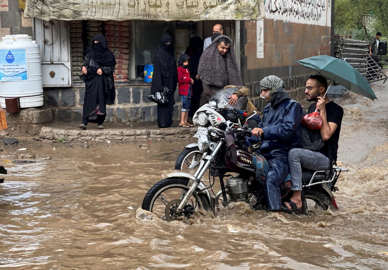 Men are seen riding a motorbike through a heavily flooded street, as women wearing burqas look on, in a street in Sanaa, yemen.