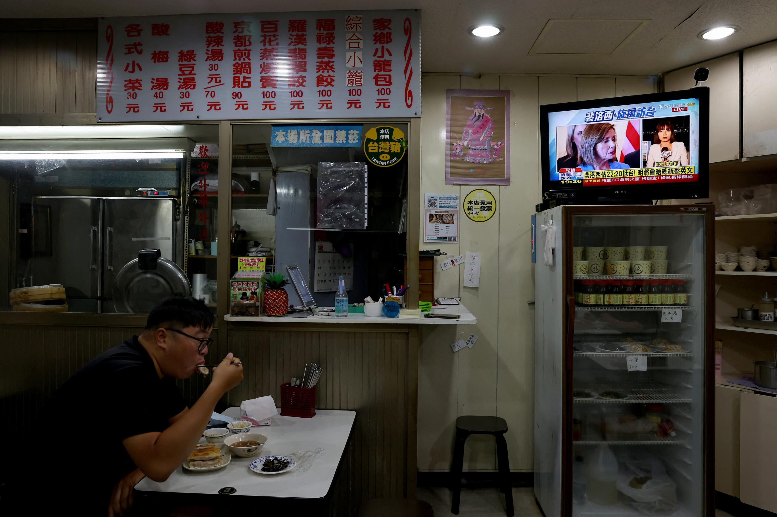 A man is photographed eating by himself at a dinner in Taipei, Taiwan, as a TV in the background displays footage of Nancy Pelosi's visit to the island