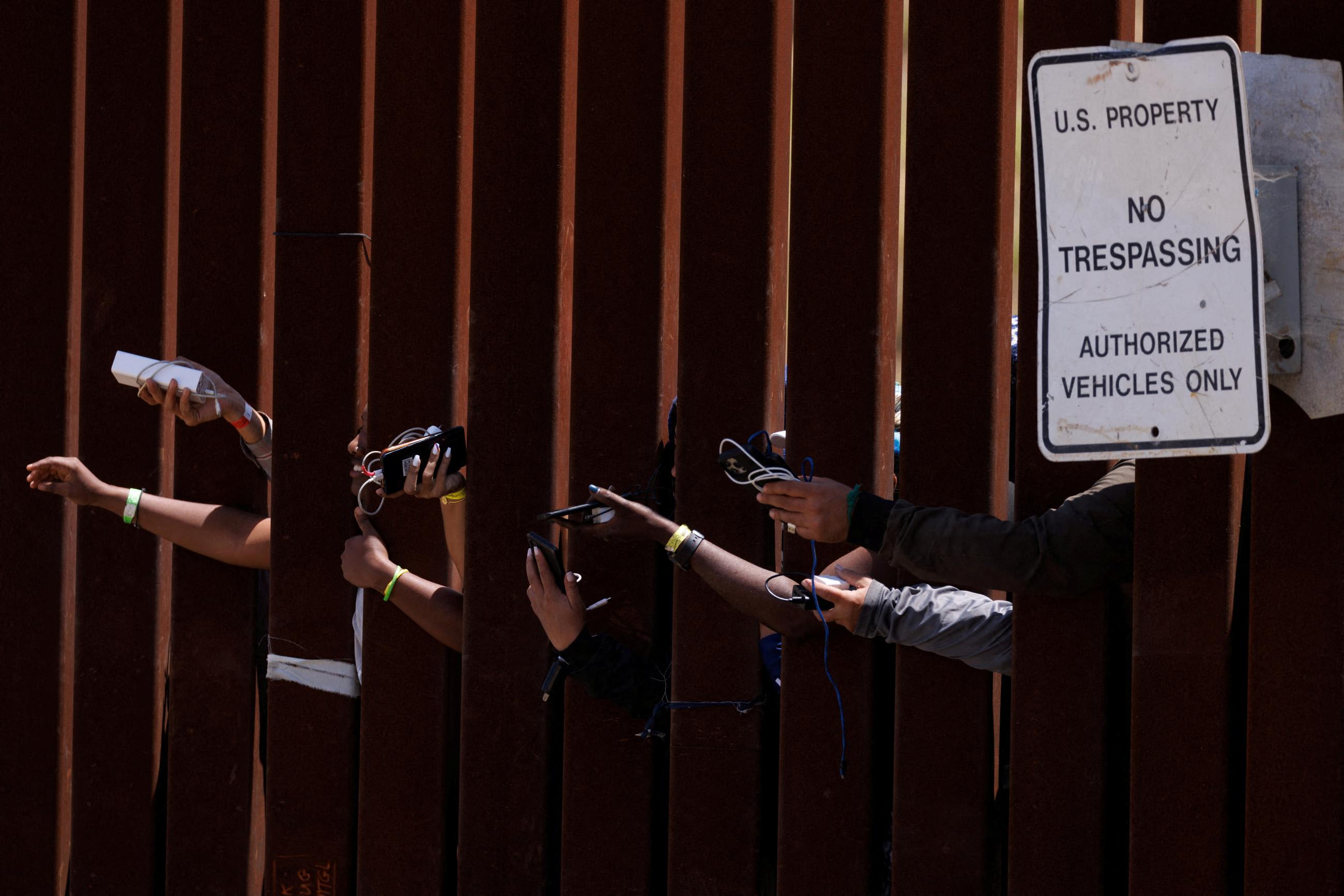 Migrants hope to get their phones charged by aid workers while they wait between border fences near San Diego, California, on May 11, 2023.