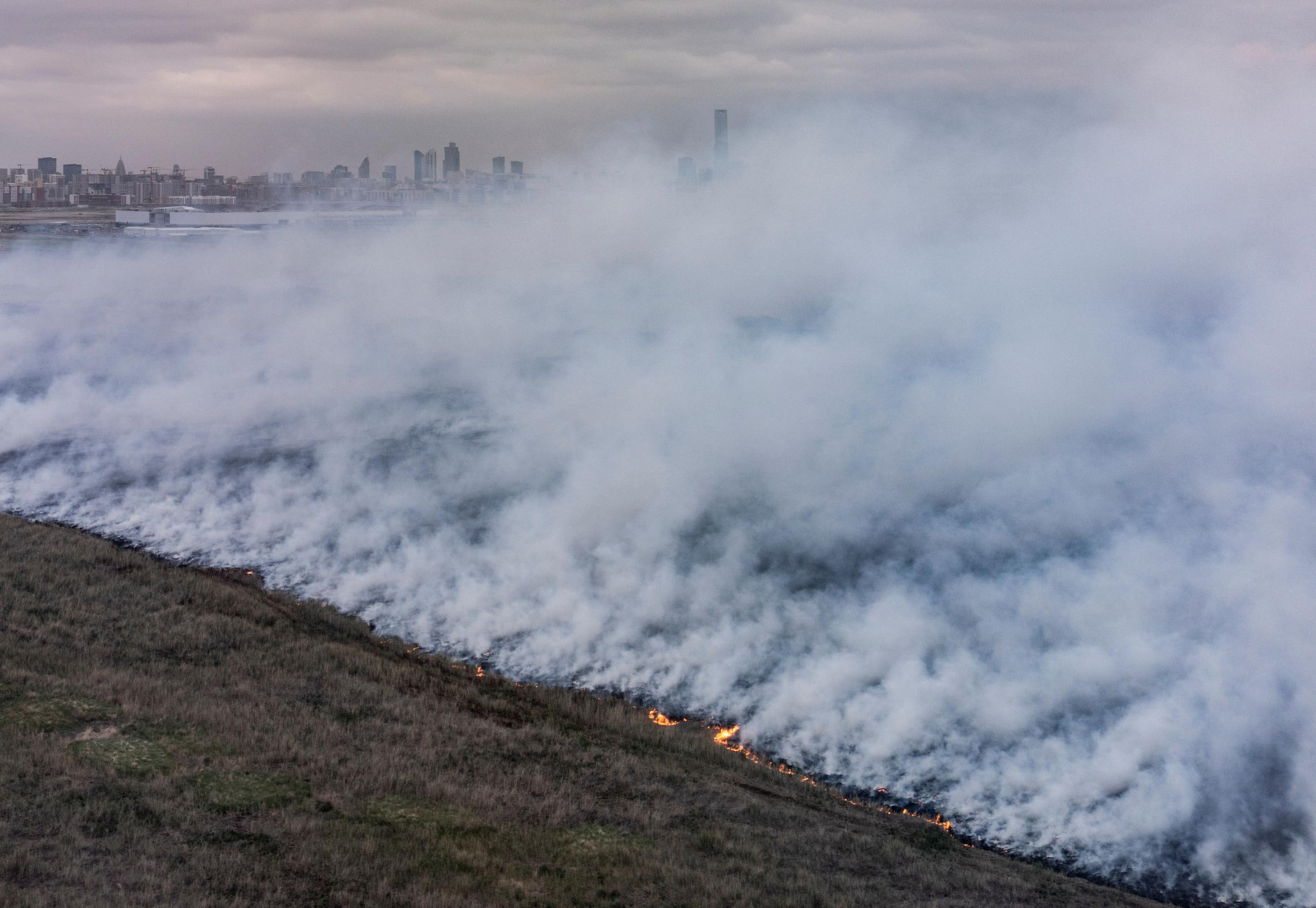 An aerial view shows smoke from a wildfire rising above a steppe against the backdrop of the capital Astana, Kazakhstan, June 19, 2023.