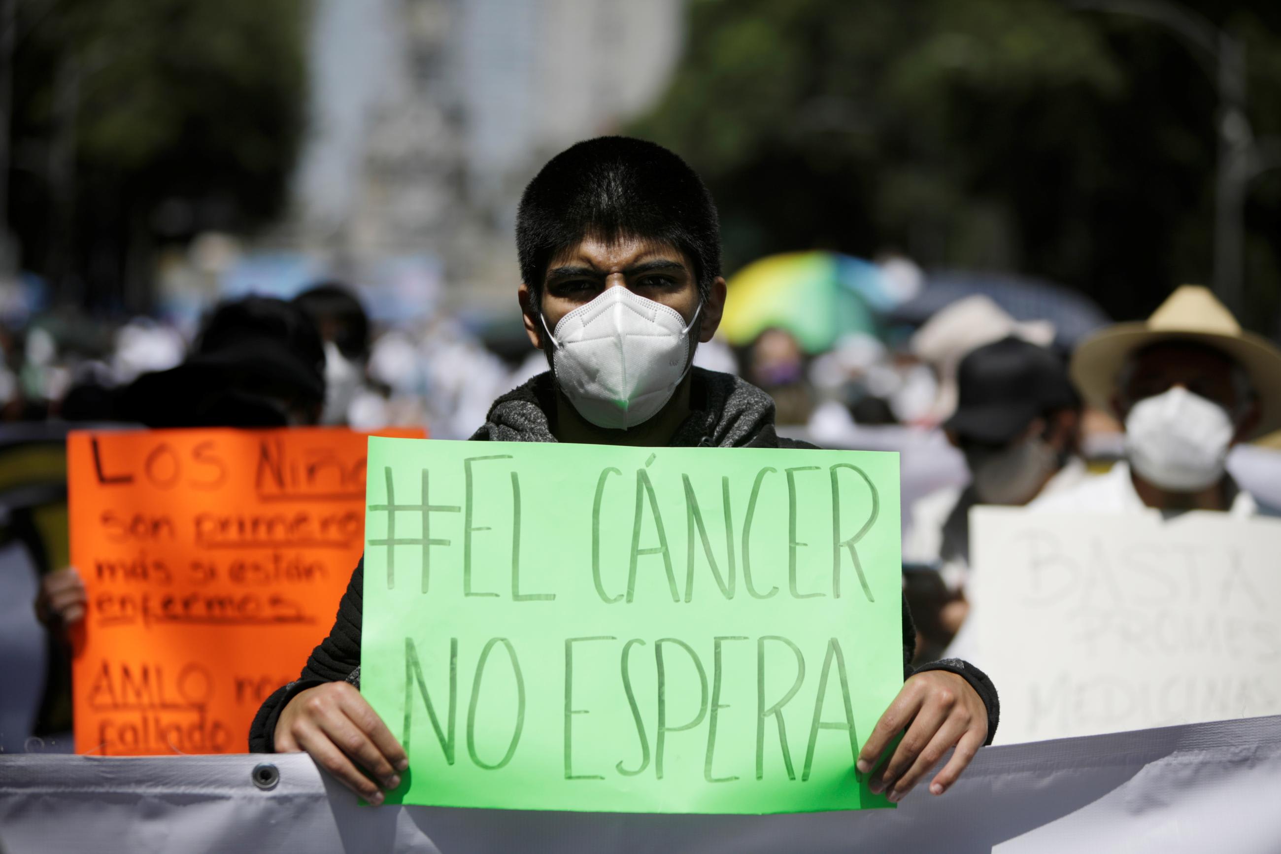 A youth with sunglasses and a face mask holds a sign that reads "cancer doesn't wait" in Spanish at a march in support of children and women with cancer in Mexico City, Mexico.