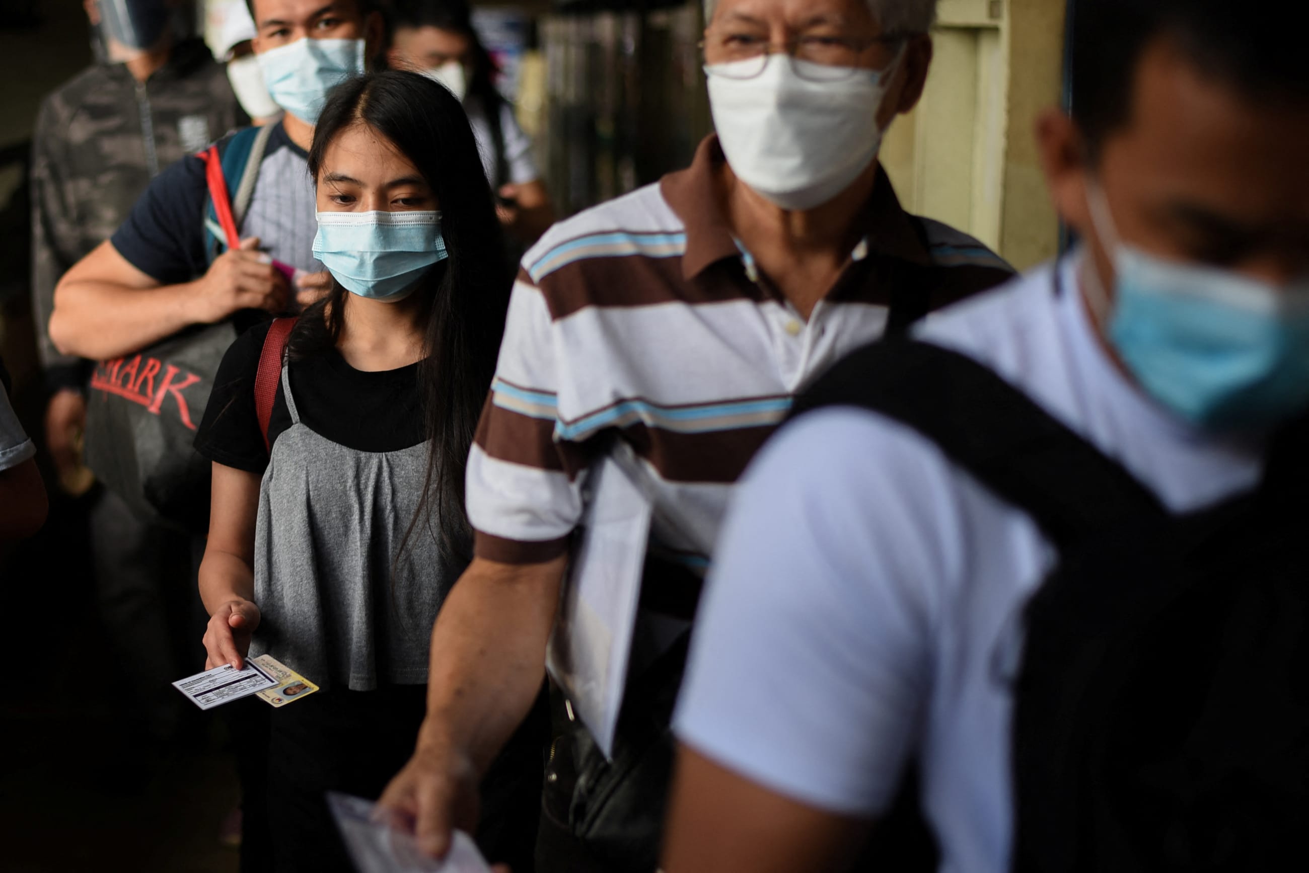 People wearing face masks as protection against COVID-19 prepare to present their vaccination cards, in Quezon City, Metro Manila, Philippines, on January 17, 2022.