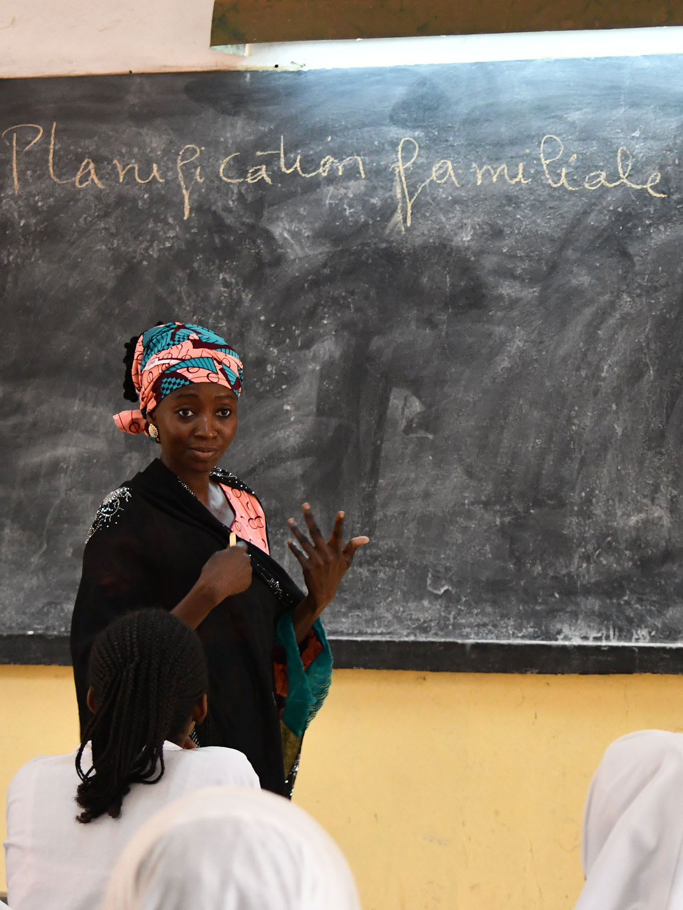 The photo shows an educator speaking to a classroom of women with the words "Planification familiale" written on the board.