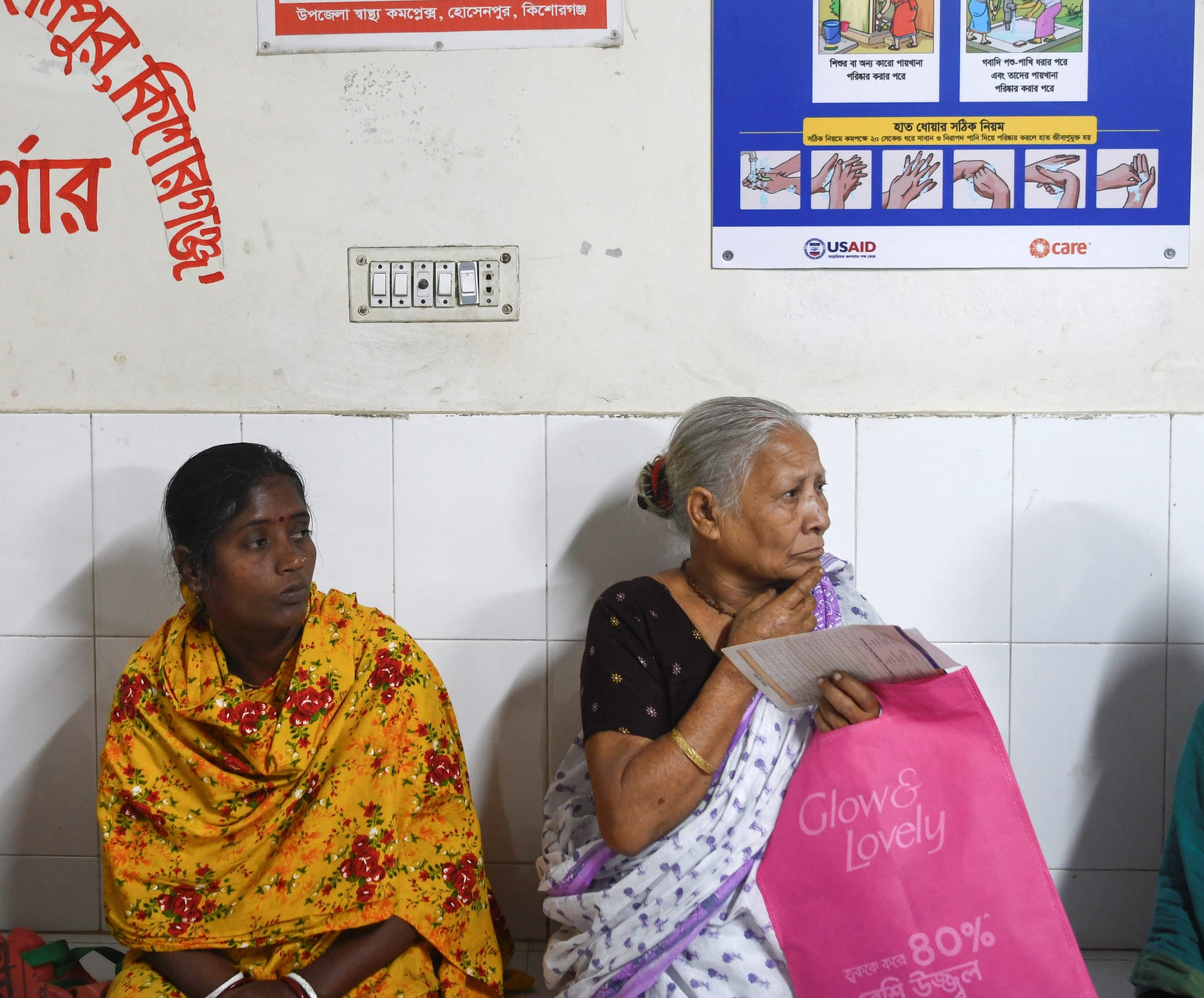 Patients wait for treatment as a USAID-funded health awareness poster hangs behind them, at the Hossainpur Upazila Health Complex, in Kishoreganj, Bangladesh, on February 10, 2025. 