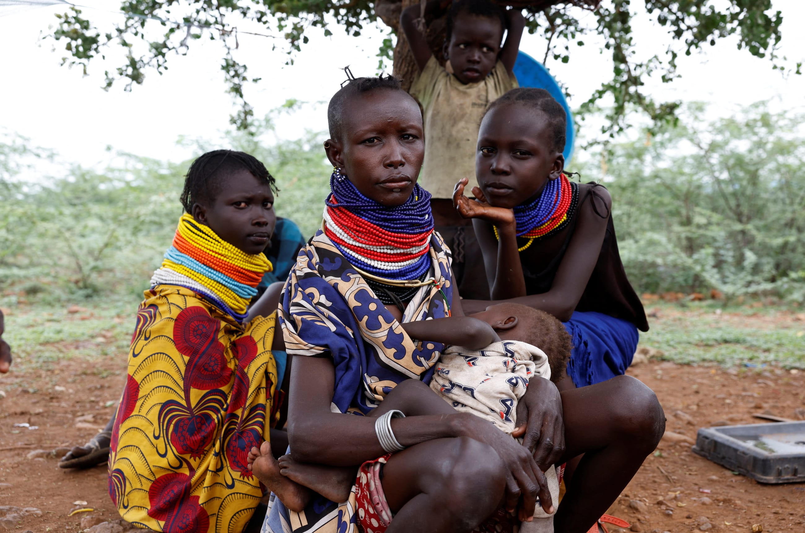 Turkana women sit under a tree as community health workers screen their children for malnutrition, in Aposta village, Turkana County, Kenya, on October 30, 2025.