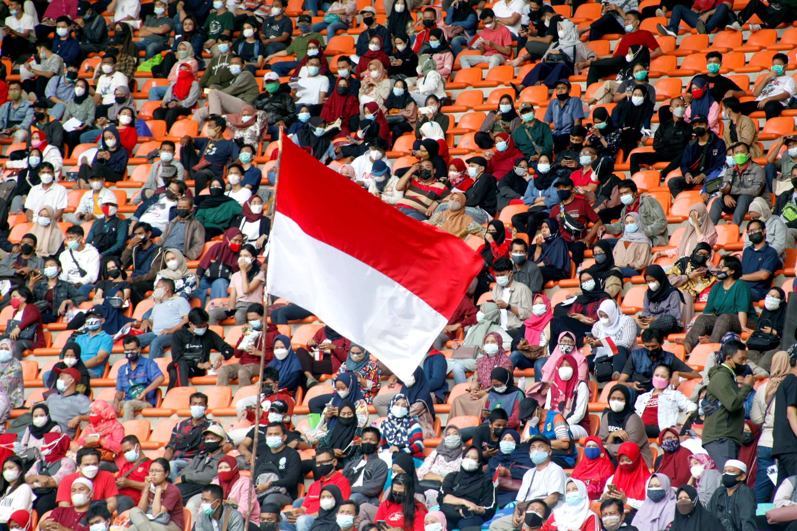 The Indonesian flag flies as people, wearing protective face coverings, wait to receive a COVID-19 vaccine dose at Pakansari Stadium, in Bogor, Indonesia, on August 14, 2021.