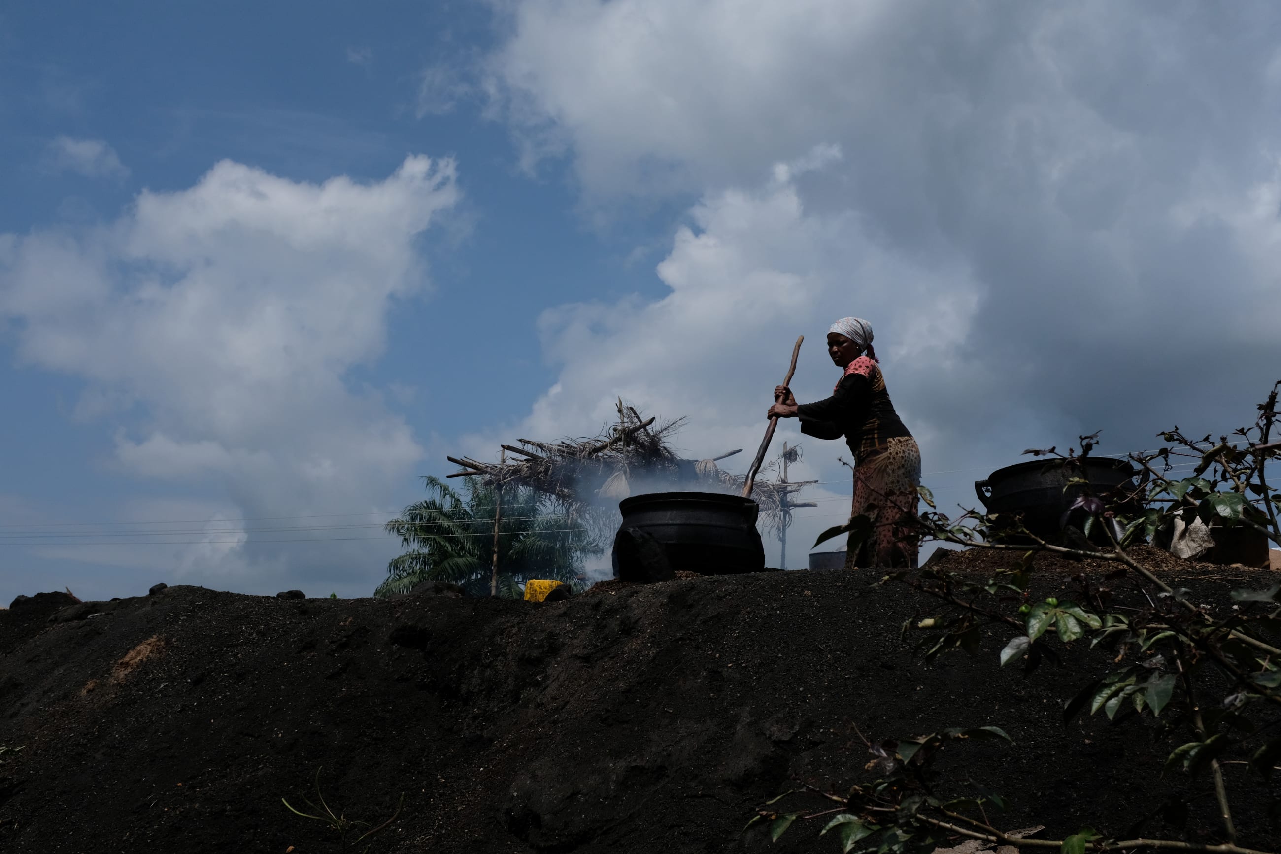 A woman cooks palm nuts to make oil on the road that connects Obuasi to Cape Coast, in Ghana, on July 26, 2019.