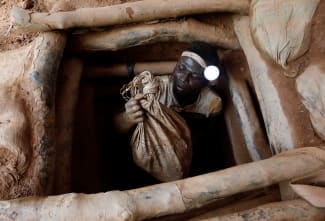 An artisanal miner climbs out of a gold mine with a bag of rocks broken off from inside a mining pit, at the unlicensed mining site of Nsuaem Top, in Ghana, on November 24, 2018.
