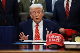 U.S. President Donald Trump sits at his desk, behind a hat that reads "America is back" at the White House, in Washington, DC, on February 3, 2026.