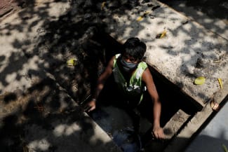 A laborer wearing a protective face mask looks on as he cleans the sewers, in New Delhi, India, on April 24, 2020.