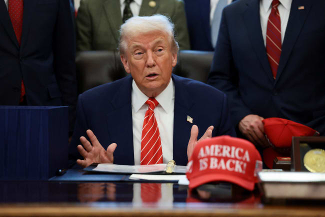 U.S. President Donald Trump sits at his desk, behind a hat that reads "America is back" at the White House, in Washington, DC, on February 3, 2026.