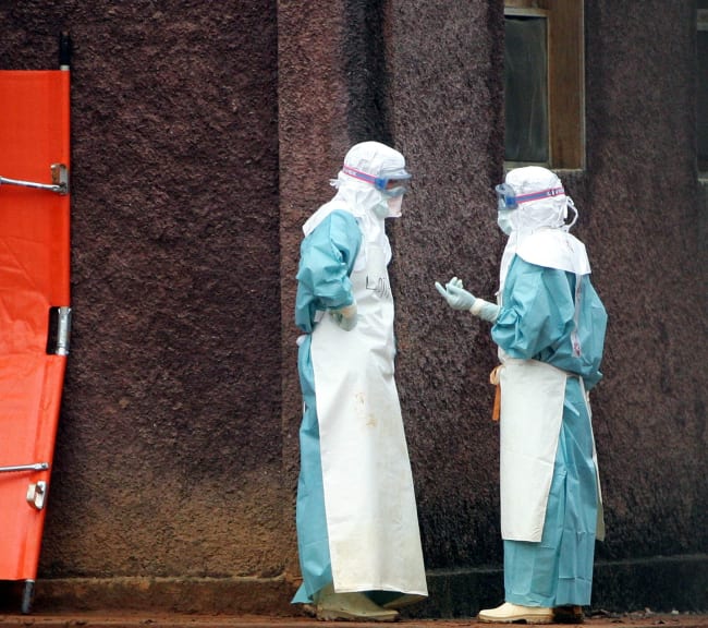 Health workers in protective clothing confer behind barriers marking the isolation ward where victims Marburg virus are treated, in Uige, Angola, on April 20, 2005.