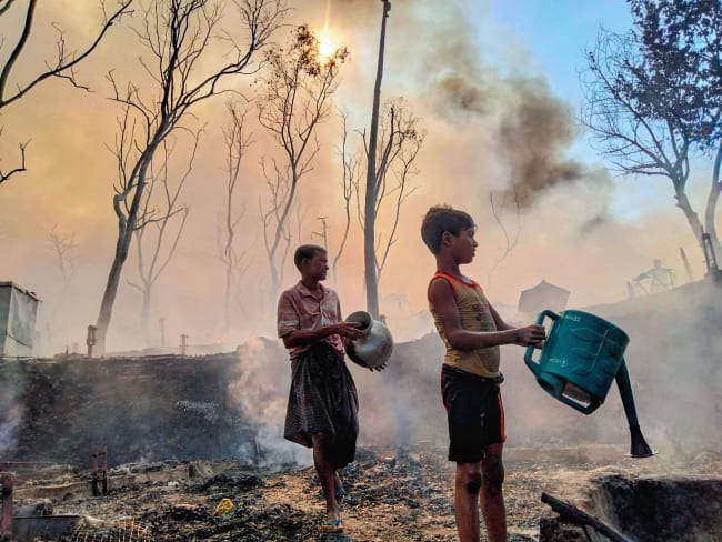 A father and son, working to reclaim what remains of a home reduced to ash, douse smoldering earth with water after a fire tore through their section of the encampment, in Cox's Bazar, Bangladesh, on December 24, 2024.