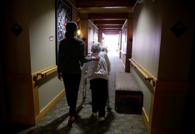 An elderly woman is guided back to her room for a family visit at Nikkei Manor, an assisted living facility, in Seattle, Washington, on March 30, 2021.