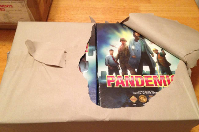 A bundle of the original Pandemic board game boxes. Photo a large armful-sized package neatly wrapped in brown paper. The paper is slightly torn open, revealing eight new boxes of the game Pandemic. Photo courtesy of Matt Leacock