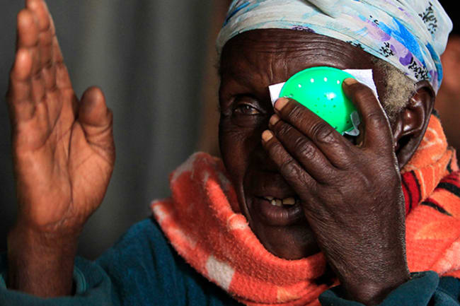 A woman at a clinic in Olenguruone, Kenya on Oct. 29, 2013 undergoes an eye exam, cataract check, and retinal scan with a technology using smartphones that uploads the data to a doctor for analysis. The photo shows a mature woman wearing a bright orange scarf taking an eye test, holding a green patch to her left eye and raising her right hand in front of her face. REUTERS/Noor Khamis 