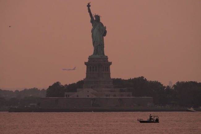 The Statue of Liberty is seen at sunset through haze caused by smoke from Canadian wildfires, as viewed from Brooklyn, New York, August 5, 2025.