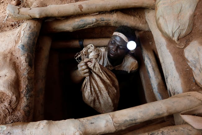An artisanal miner climbs out of a gold mine with a bag of rocks broken off from inside a mining pit, at the unlicensed mining site of Nsuaem Top, in Ghana, on November 24, 2018.