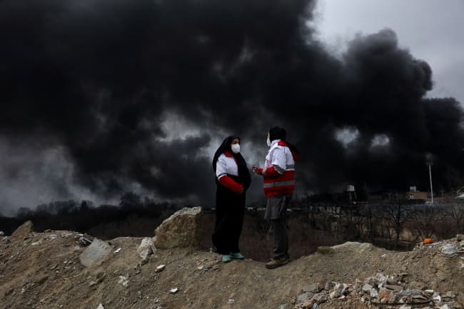 Members of the Red Crescent talk to each other as smoke rises into the air after a reported strike on Shahran fuel tanks, in Tehran, Iran, on March 8, 2026.