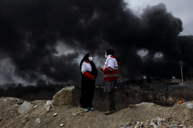 Members of the Red Crescent talk to each other as smoke rises after a reported strike on Shahran fuel tanks, amid the U.S.-Israeli conflict with Iran, in Tehran, Iran, March 8, 2026.