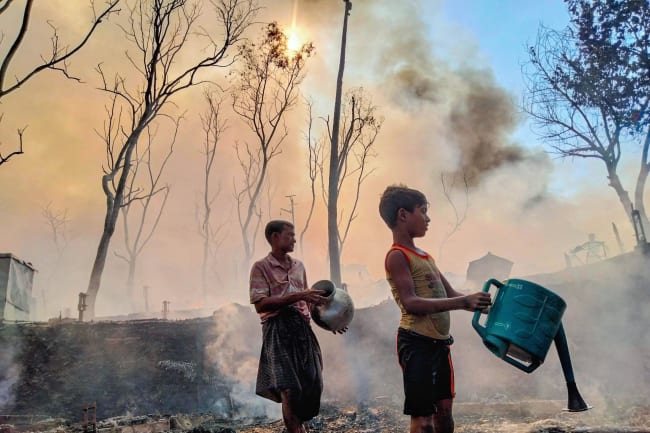 A father and son, working to reclaim what remains of a home reduced to ash, douse smoldering earth with water after a fire tore through their section of the encampment, in Cox's Bazar, Bangladesh, on December 24, 2024.