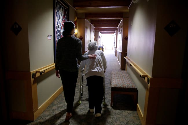 An elderly woman is guided back to her room for a family visit at Nikkei Manor, an assisted living facility, in Seattle, Washington, on March 30, 2021.