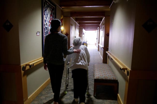 An elderly woman is guided back to her room for a family visit at Nikkei Manor, an assisted living facility, in Seattle, Washington, on March 30, 2021.