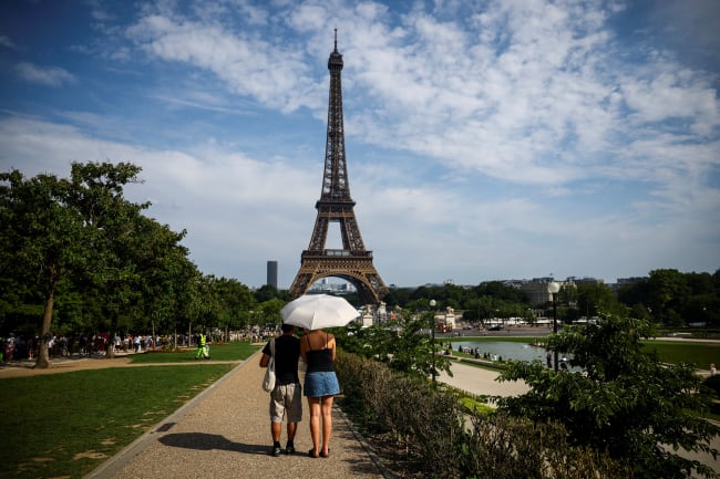 People protect themselves from the sun under an umbrella near the Eiffel Tower during a heatwave, in Paris, France, on June 20, 2026.