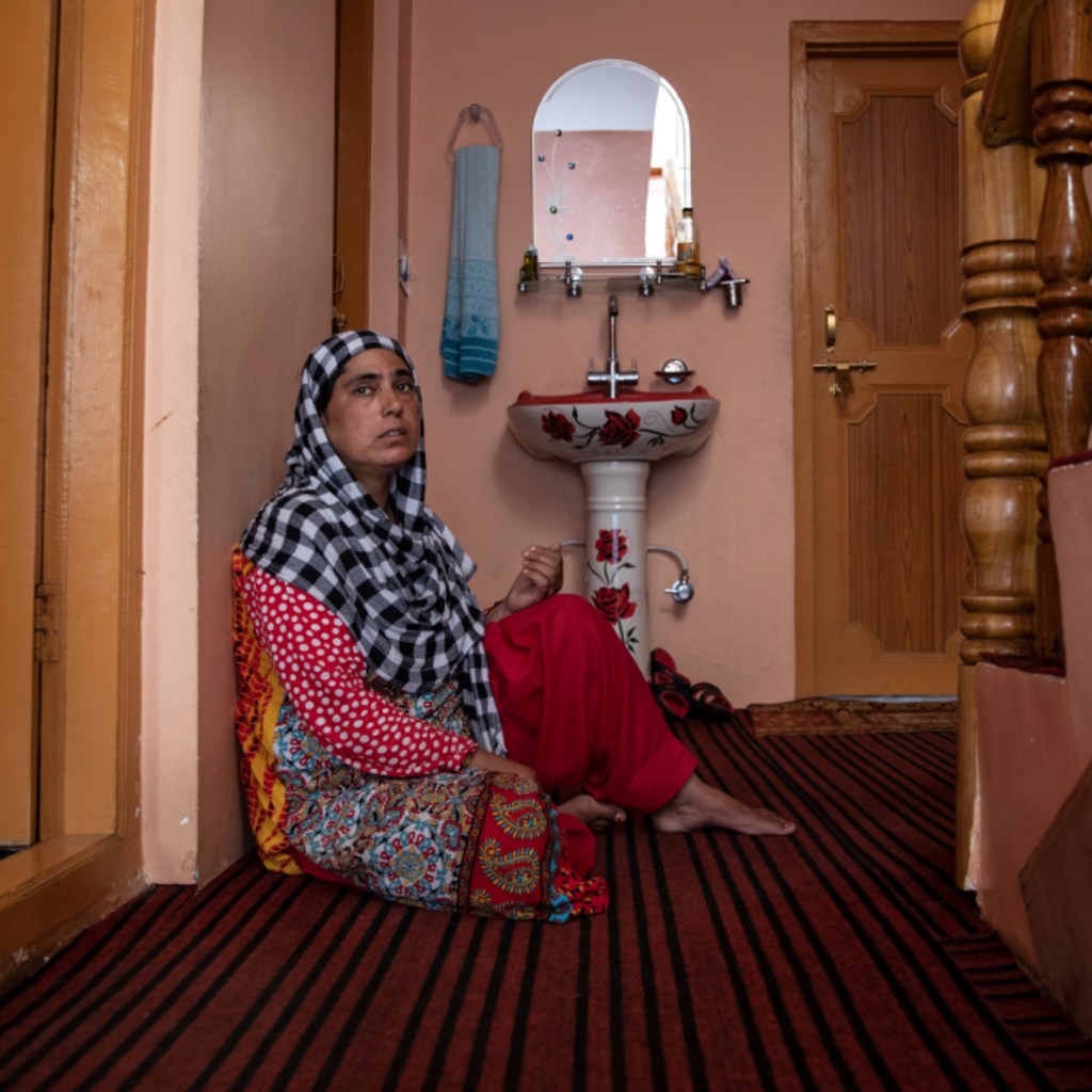 <p>A woman sits in the doorway of her home in Pulwama.</p>