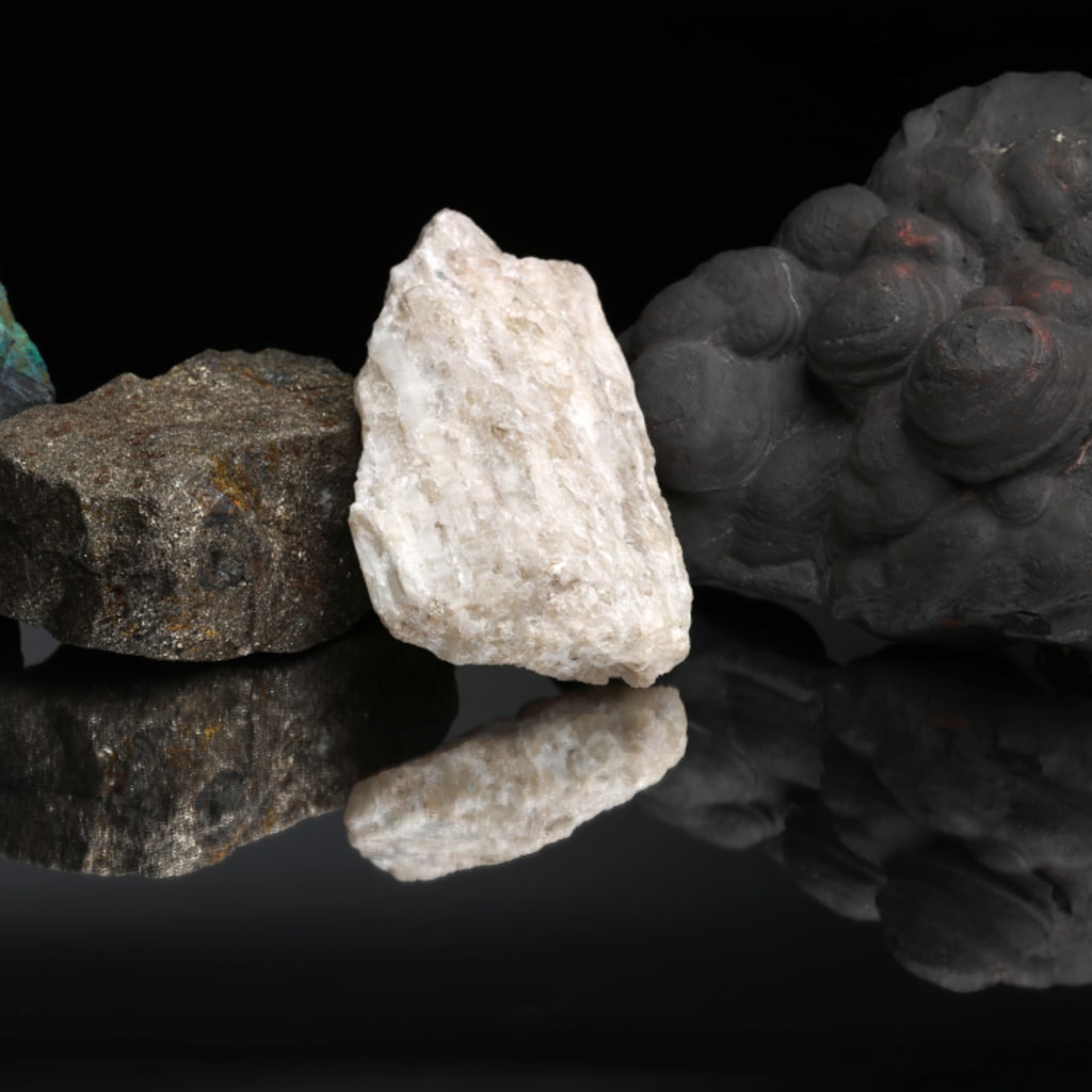 Critical mineral ores, including copper, graphite, nickel, lithium, and manganese, against a black background and reflected on a mirrored table.