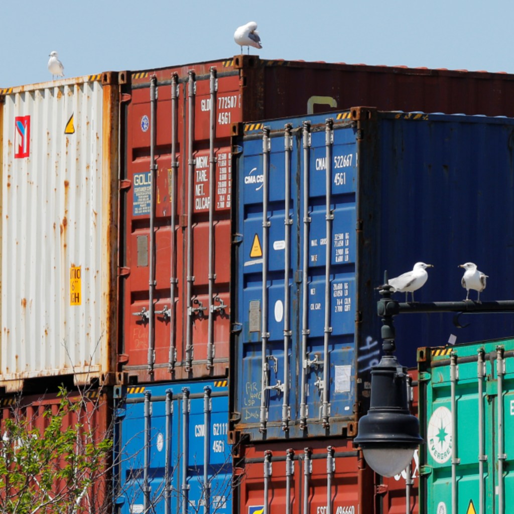 Sea gulls sit on a lamppost beside shipping containers stacked at the Paul W. Conley Container Terminal in Boston
