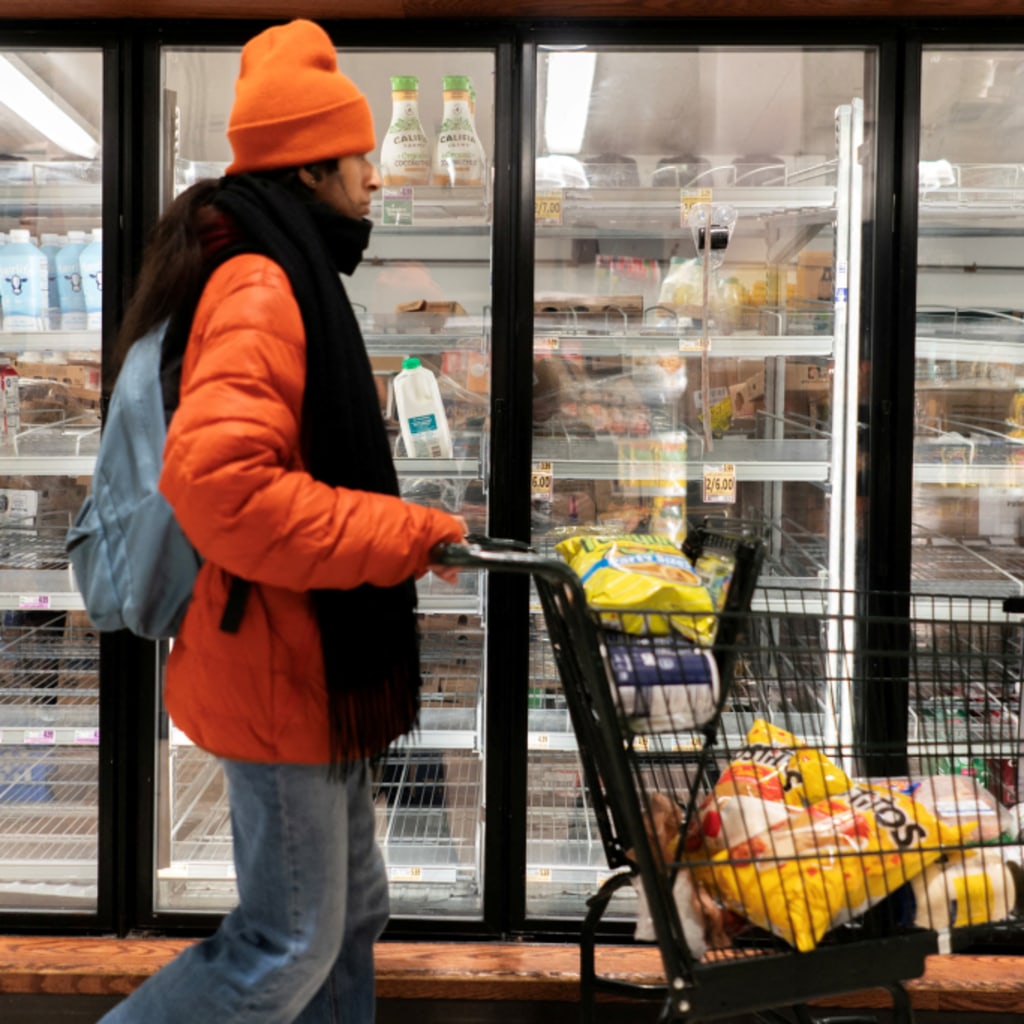 A shopper walking past a partially empty dairy section of a grocery store