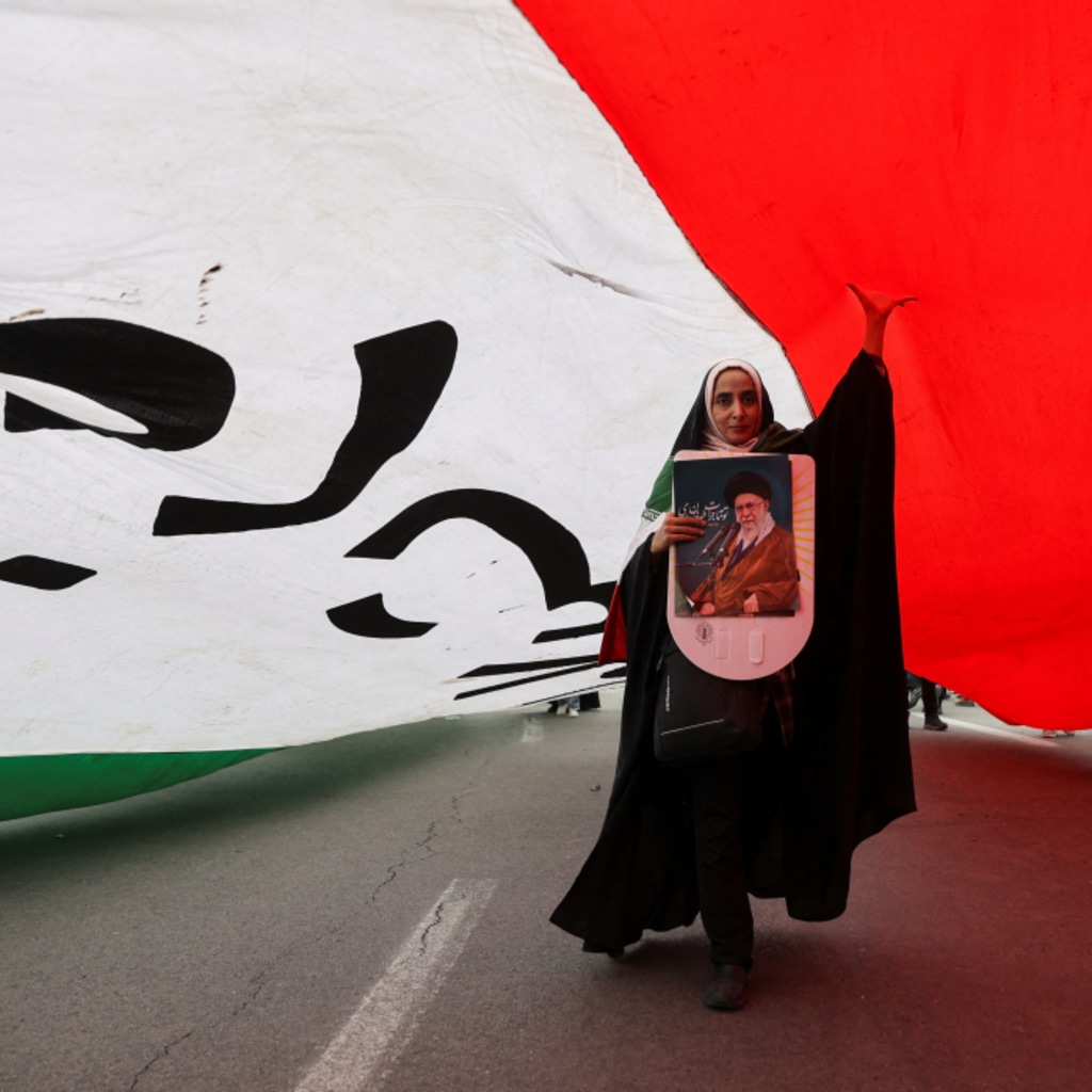 An Iranian woman holding a poster depicting Iran's Supreme Leader Ayatollah Ali Khamenei walks under a large flag during the forty-seventh anniversary of the Islamic Revolution in Tehran, Iran on February 11, 2026. Majid Asgaripour/West Asia News Agency via Reuters