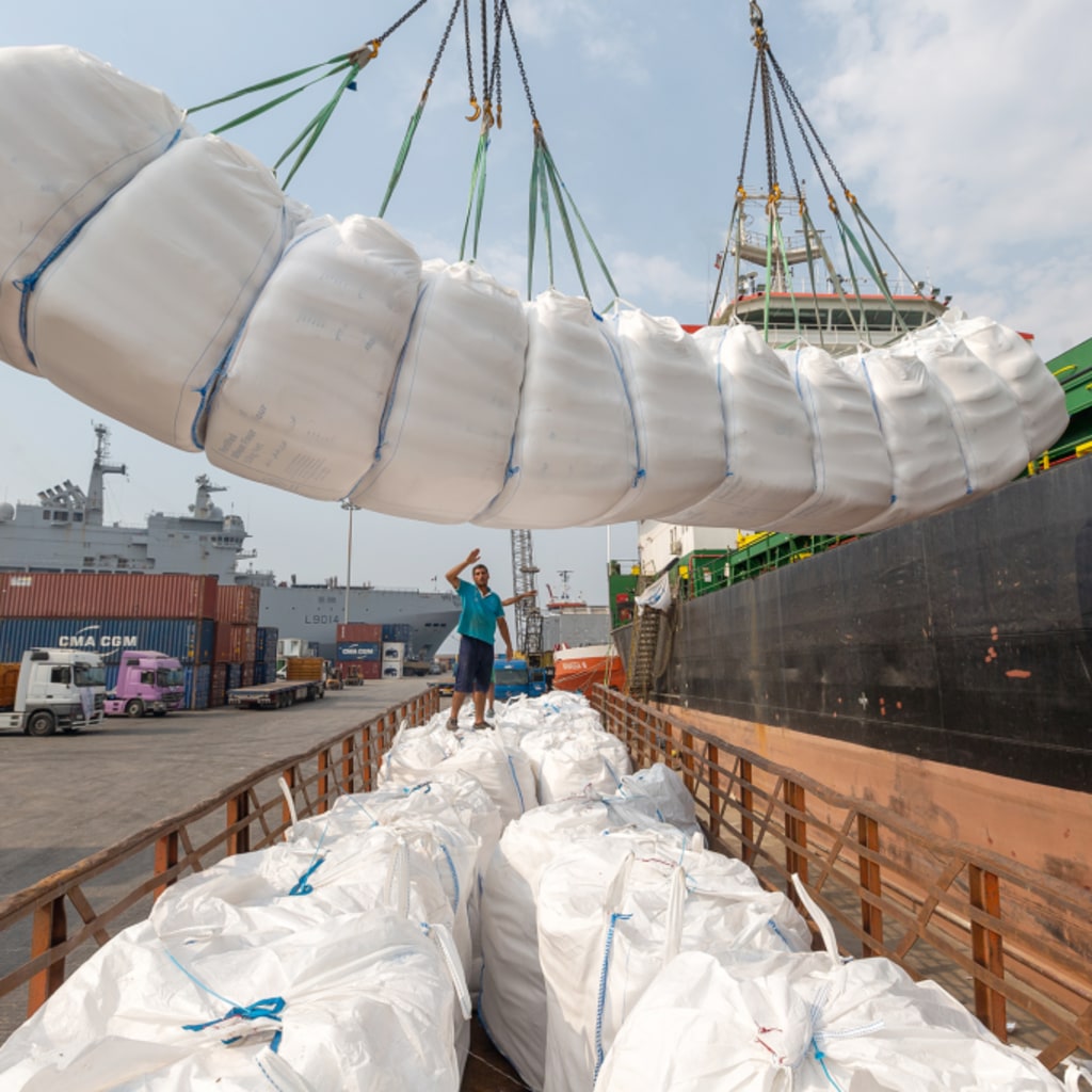 A crane lowers a white package containing food aid into a crate off of the side of a ship.