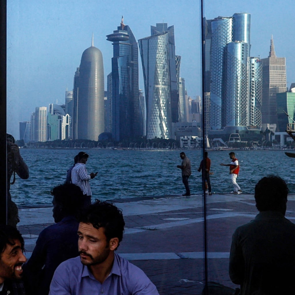 People sit with the reflection of the Doha skyline along the Doha Corniche, on the second day of Eid al-Fitr celebrations marking the end of the Muslim holy month of Ramadan, in Doha on March 21, 2026.