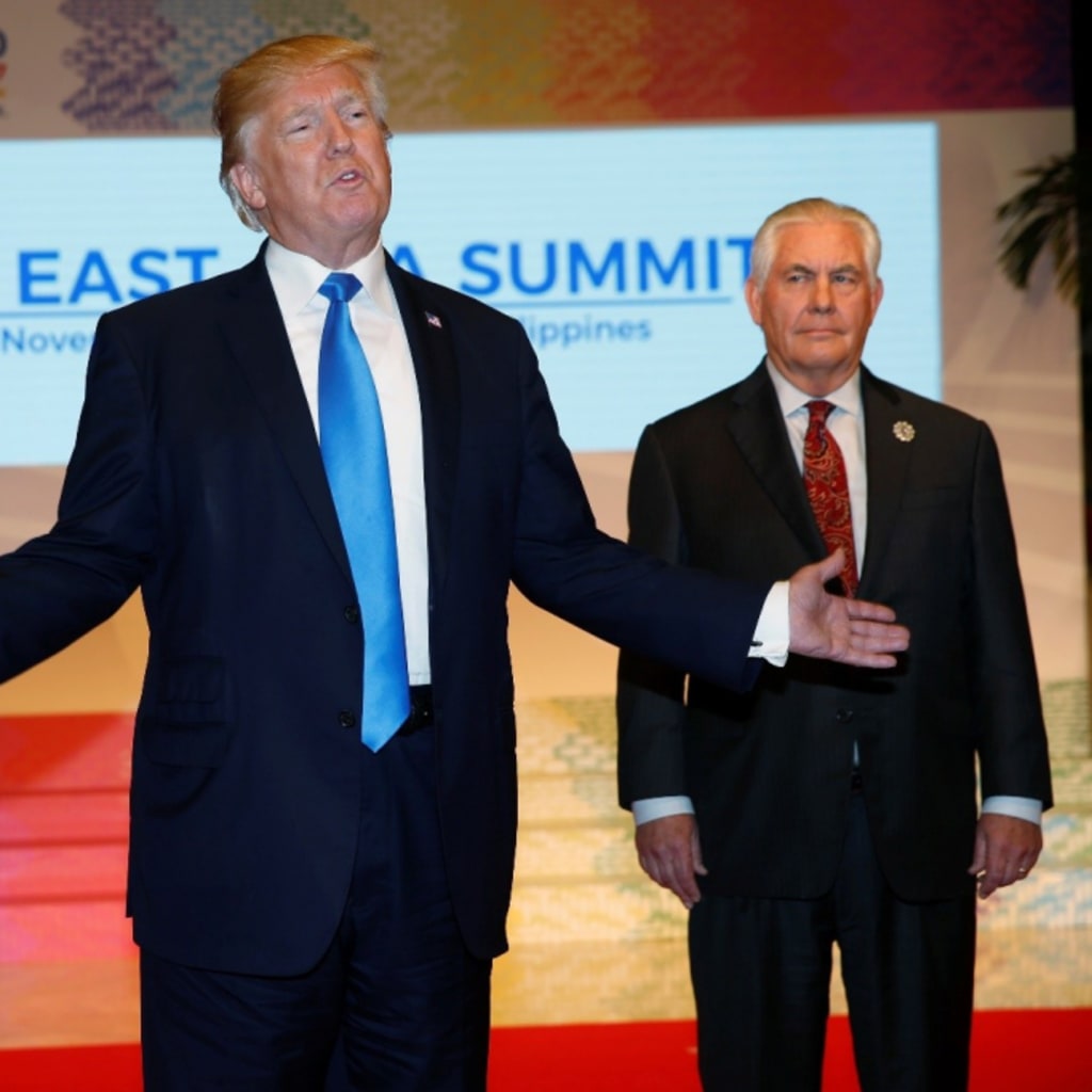 U.S. President Donald Trump stands between two aides in front of projected signage reading "12th East Asian Summit"