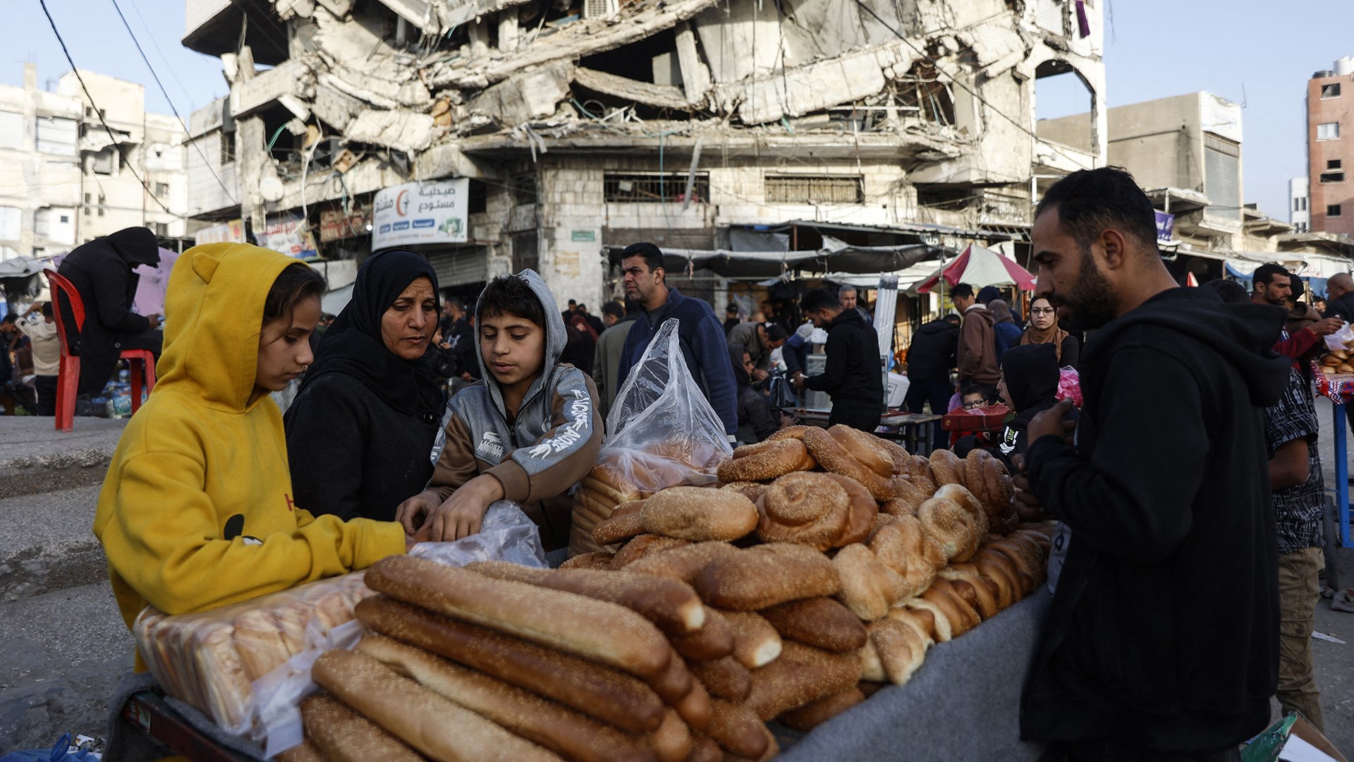 Palestinians sell bread on a street beneath a destroyed building in Gaza City's Zawiya market on February 18, 2026, on the first days of the holy fasting month of Ramadan.
