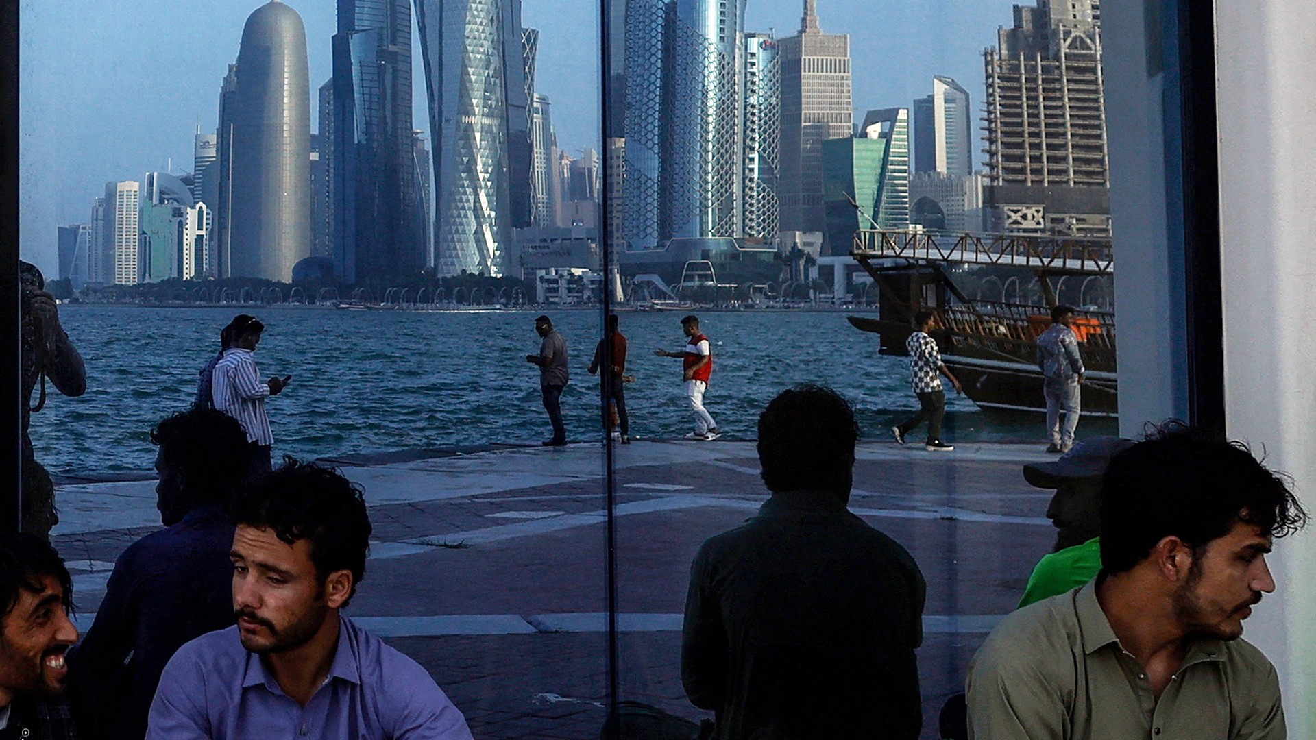 People sit with the reflection of the Doha skyline along the Doha Corniche, on the second day of Eid al-Fitr celebrations marking the end of the Muslim holy month of Ramadan, in Doha on March 21, 2026.