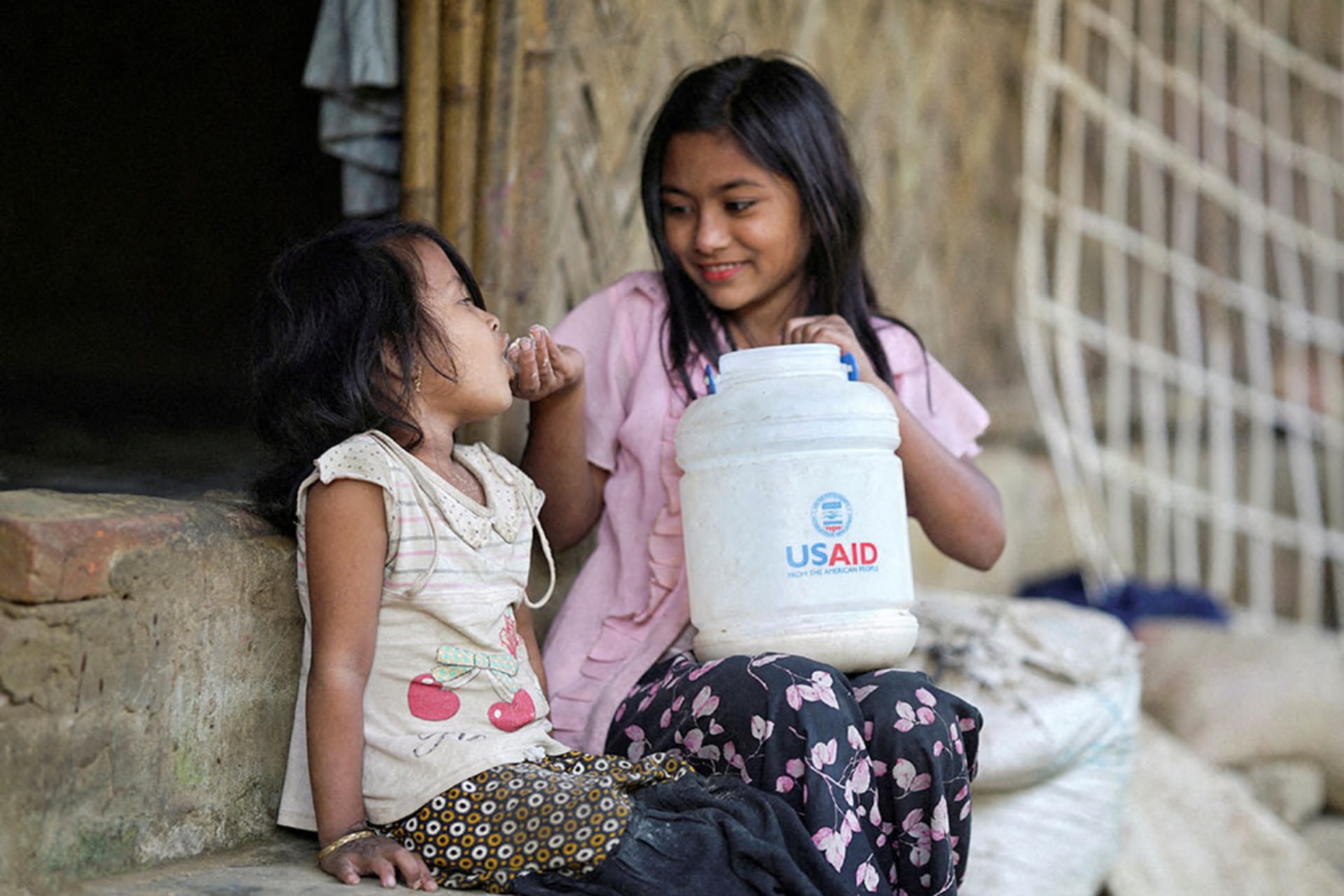<p>A Rohingya girl feeds a child from a jar with the USAID logo on it, at a refugee camp in Cox’s Bazar, Bangladesh, February 11, 2025. </p>