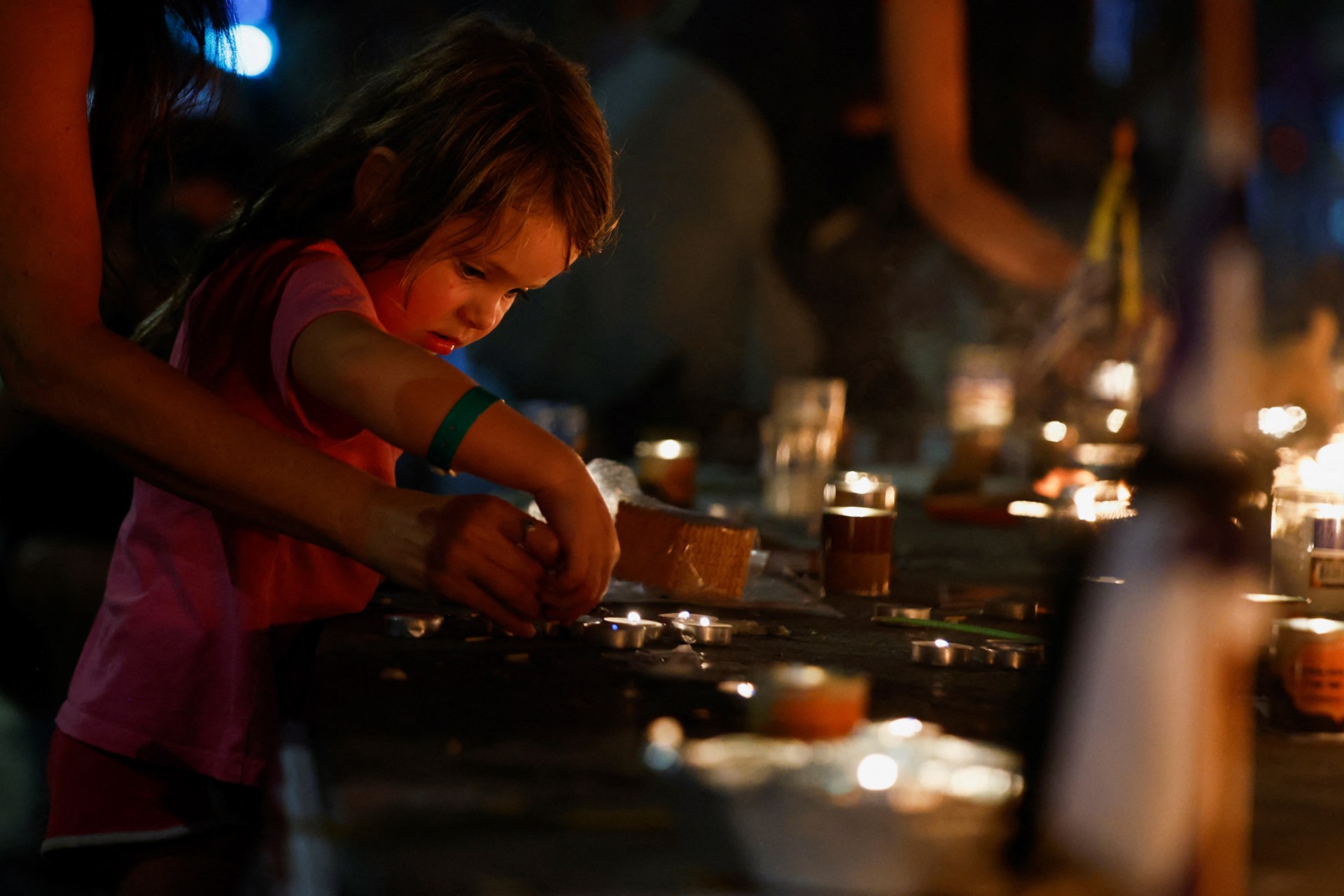 <p>A girl helps to light a candle, as people gather for a candlelit vigil to mark the one-month anniversary of the October 7 deadly attack by Palestinian Islamist group Hamas on Israel, in Tel Aviv, Israel, November 7, 2023.</p>