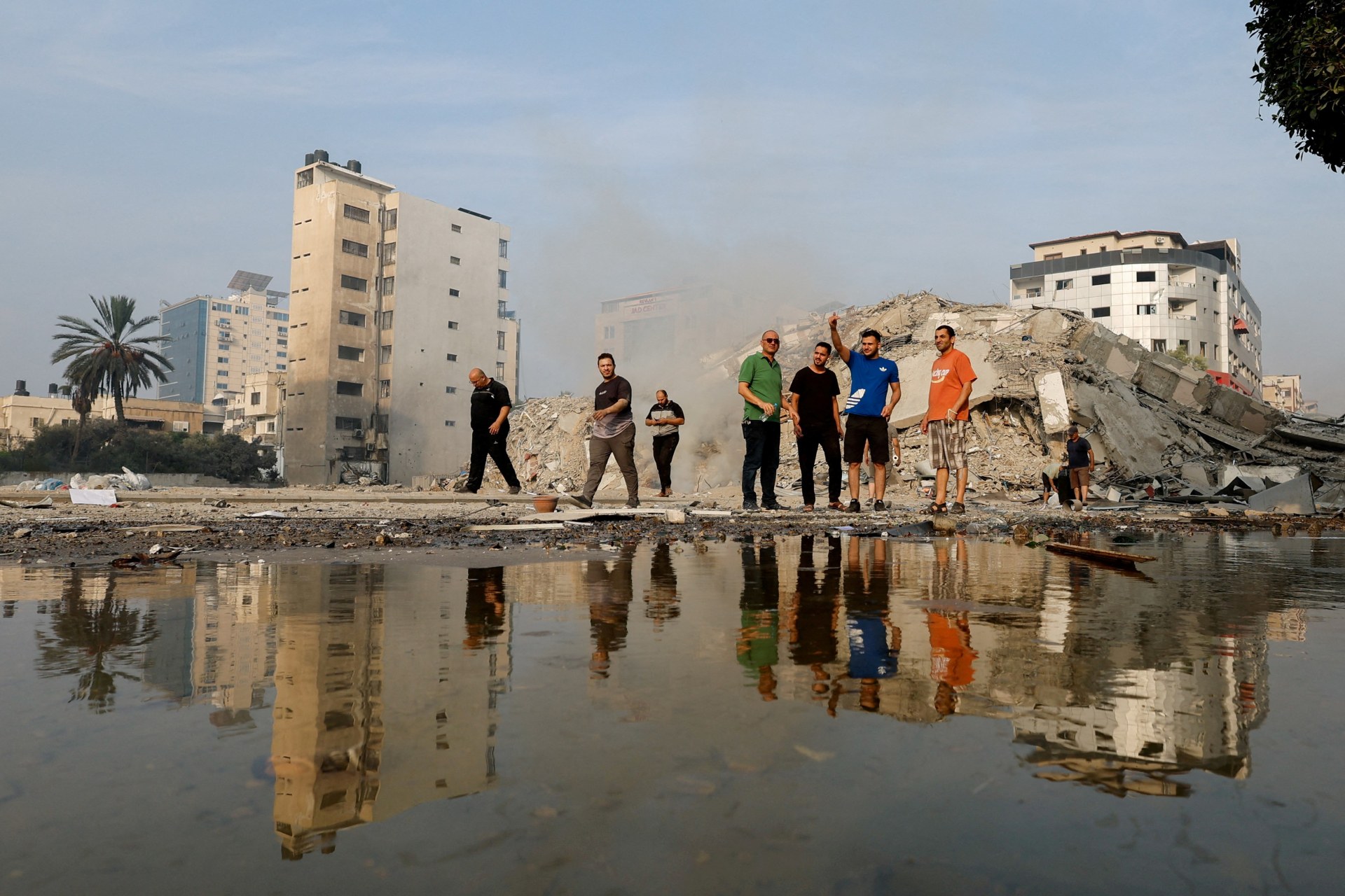 <p>Palestinians inspect the ruins of Watan Tower, which was destroyed in Israeli strikes, in Gaza City</p>