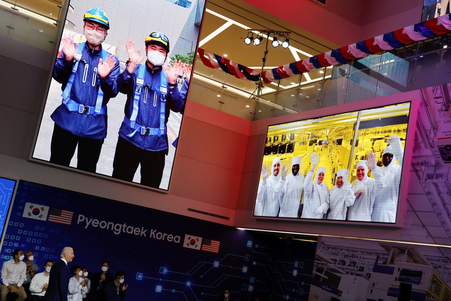 <p>Samsung employees are displayed on screens as they gesture during U.S. President Joe Biden’s visit to a semiconductor factory at the Samsung Electronics Pyeongtaek Campus in Pyeongtaek, South Korea in May 2022.</p>

